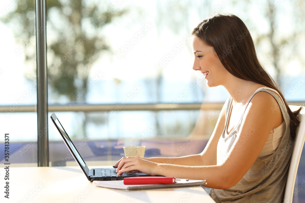 Happy woman typing on laptop in a coffee shop table