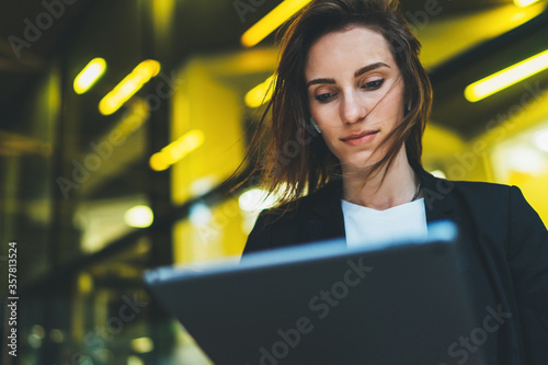 professional female finance lawyer standing near office in evening street communicates online by tablet. Businesswoman pushing message to colleagues using computer on background yellow neon lights