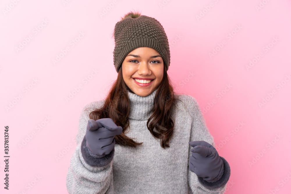 Young Colombian girl with winter hat over isolated pink wall points finger at you Young Colombian girl with winter hat over isolated pink wall points finger at you