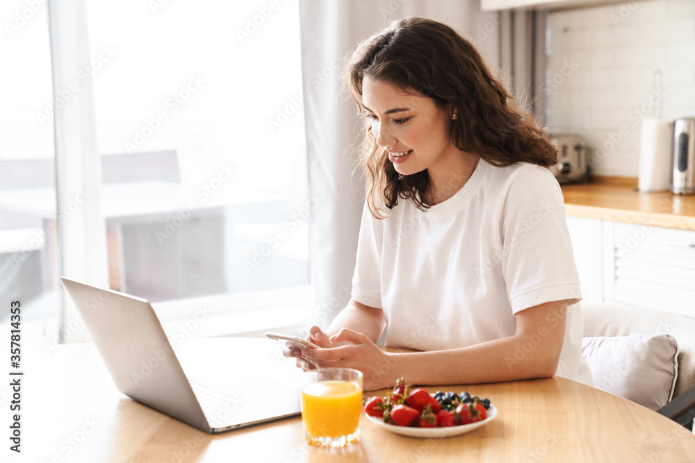 Photo of woman using laptop and mobile phone while having breakfast