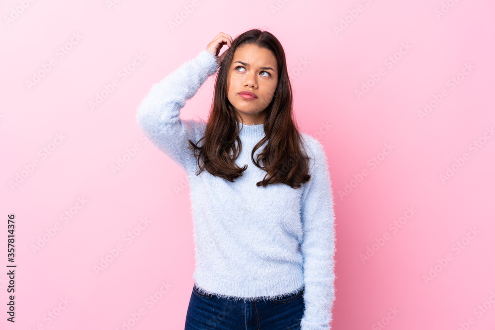 Young Colombian girl over isolated pink background having doubts and with confuse face expression Young Colombian girl over isolated pink background having doubts and with confuse face expression
