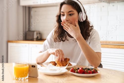Photo of woman watching movie on mobile phone while having breakfast