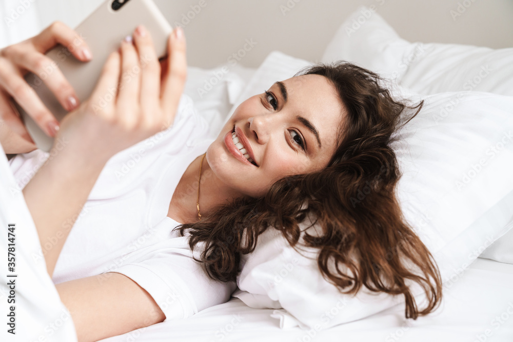 Fototapeta premium Photo of cheerful woman taking selfie on cellphone while lying on bed