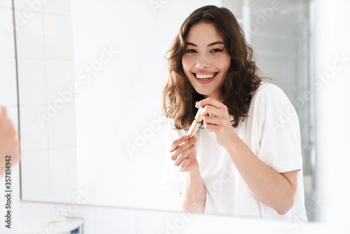 Fototapeta Naklejka Na Ścianę i Meble -  Photo of woman smiling and holding mascara while looking at mirror