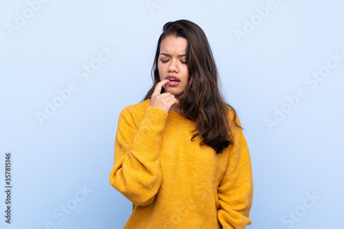 Young Colombian girl with sweater over isolated blue background nervous and scared