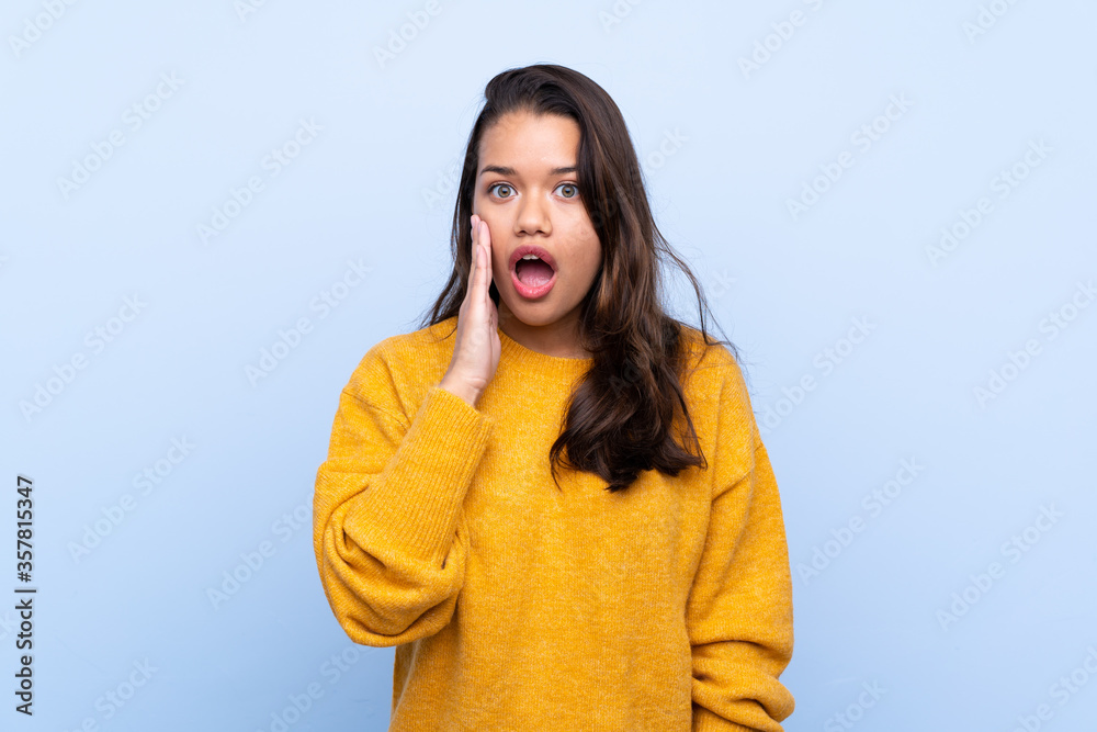 Young Colombian girl with sweater over isolated blue background with surprise and shocked facial expression