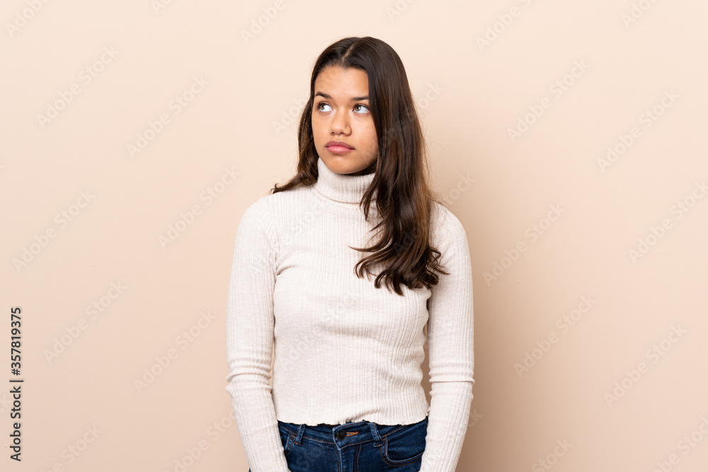 Young Colombian girl over isolated background making doubts gesture looking side Young Colombian girl over isolated background making doubts gesture looking side