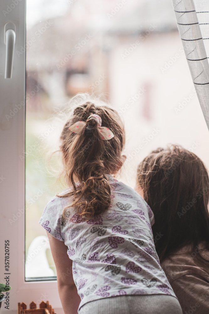 Two girls are looking out the window at a white dove sitting on a windowsill behind a glass.