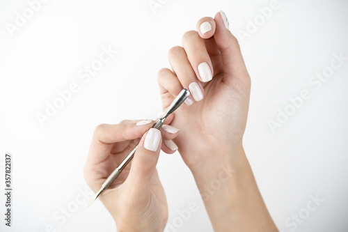 picture of hands using cuticle pusher while doing manicure on isolated while background