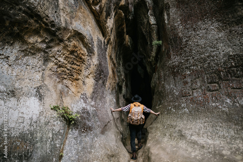 A young male amateur speleologist enters a mountain cave with a backpack photo