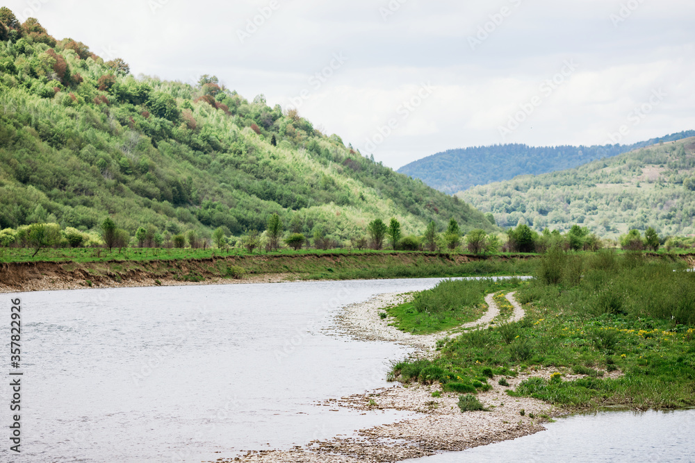 Mountain river among green hills with forest and grass