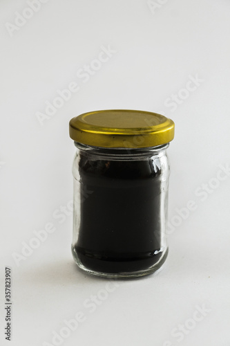Small Glass Jar of Dark Honey with Metallic Cap isolated on a white background.