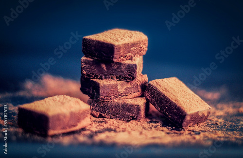 Homemade Chocolate Pieces Stack sprinkled with Cocoa Powder on a dark background. Handcrafted Chocolate Concept. Selective Focus.