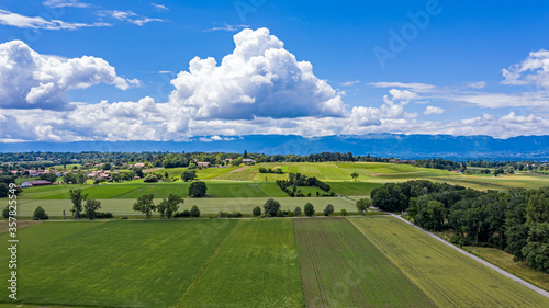 Aerial drone shot of the countryside and farm land around the area of Geneva, Switzerland. The large white clouds and blue sky and green fields of this picturesque landscape.