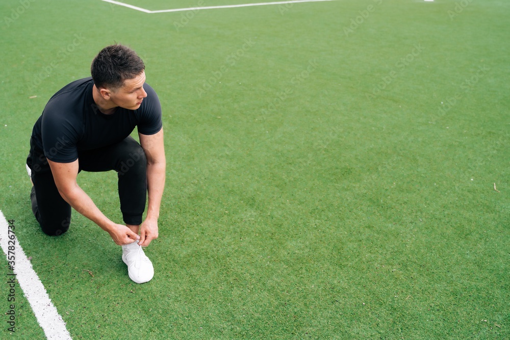 A handsome young male fitness trainer in sportswear tilted to tie his shoelaces on his sneakers. The concept of safe training A handsome young male fitness trainer in sportswear tilted to tie his shoelaces on his sneakers. The concept of safe training