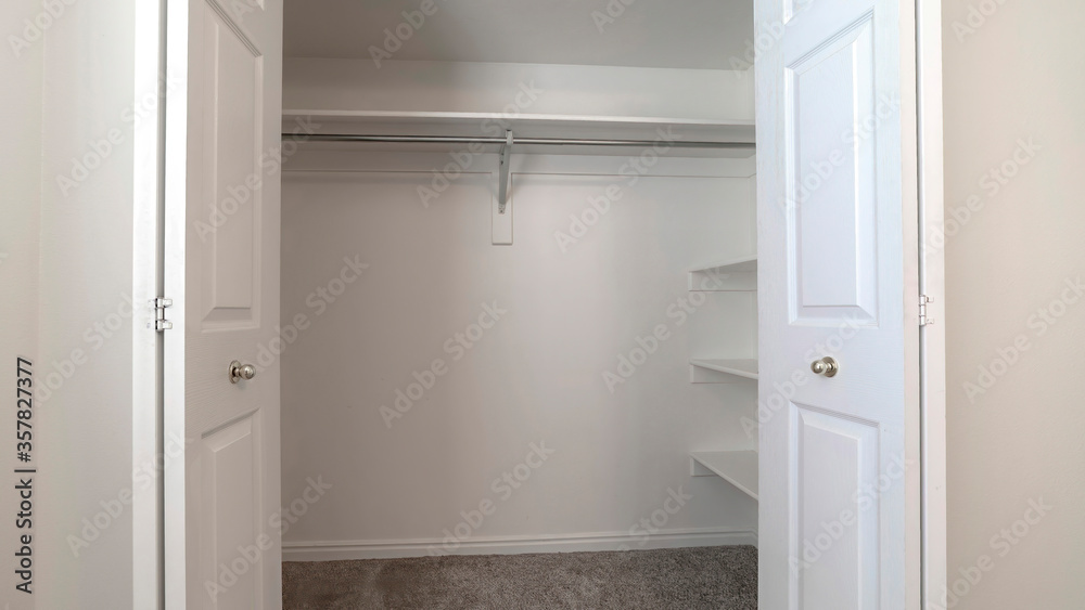 Panorama Walk in closet with double hinged doors plain white wall and gray floor carpet Panorama Walk in closet with double hinged doors plain white wall and gray floor carpet