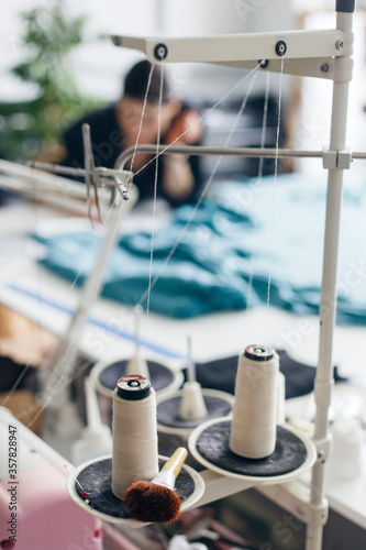 Spools of thread on an overlock machine in foreground and designer working on background. The concept of a professional sewing workshop. Clothing designer tools.
