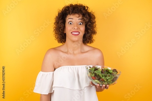 Young beautiful girl  holding a salad with an afro hairstyle having broad white smile being excited to meet Friends and go out to have a good day.