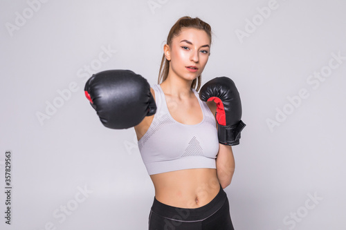Portrait of young woman boxer throwing a punch at camera while practicing on grey background. Mixed race female athlete wearing boxing gloves exercising boxing. © dianagrytsku
