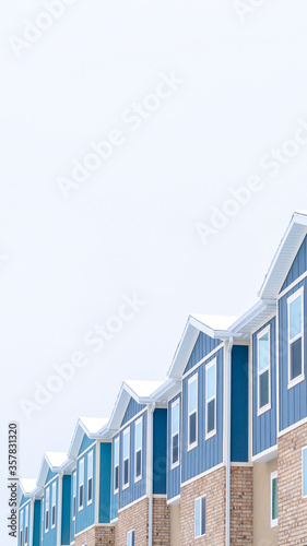 Vertical crop Snowy gable roofs at the facade of townhome with brick wall and vertical siding