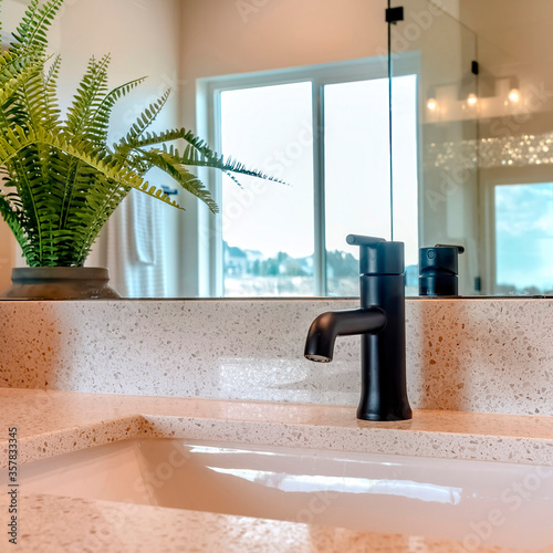 Square Undermount single basin sink on counterop with black faucet and potted plant photo