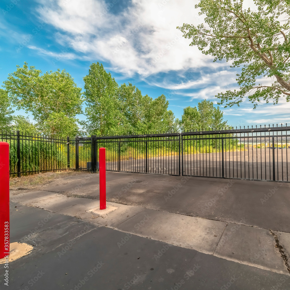 Square Private gate at a secured property with red traffic poles on the paved gray road Square Private gate at a secured property with red traffic poles on the paved gray road