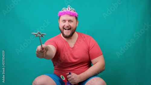 cute bearded freaky man in a pink T-shirt with a diadem on his head dreams of riding a unicorn with a magic wand in his hand. A funny wizard joke to make and fulfill a wish