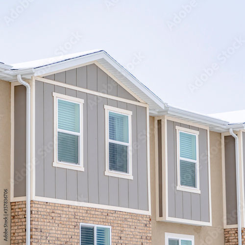 Square Snowy roof brick wall and vertical siding at exterior of townhome against sky © Jason