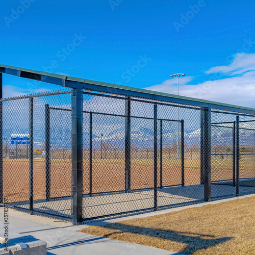 Square Baseball field dugout with slanted roof and chain link fence on a sunny day © Jason