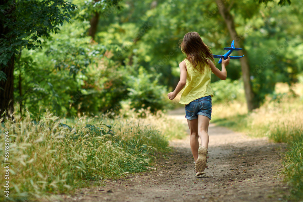 The concept of dreams and travel. Happy girl kid playing with toy airplane in summer on nature.