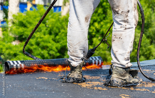 Overhaul of the roof of a living house. A construction worker using a gas burner puts waterproofing material. Fire in the frame.