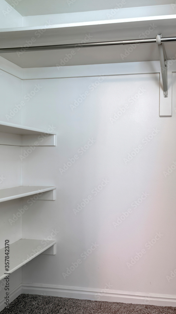 Vertical Empty walk in closet of new home with wall shelves and hanging ...