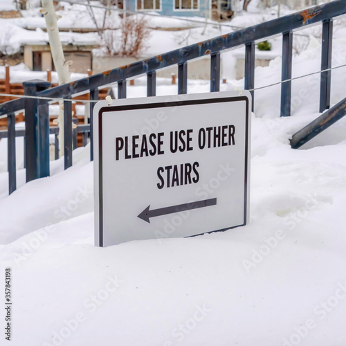 Square crop Stairs buried in winter snow with sign that reads Please Use Other Stairs