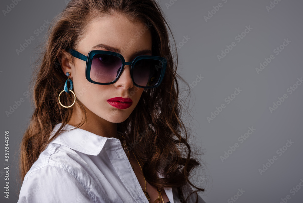 Fashionable model, woman wearing trendy big square sunglasses with blue plastic frame, stylish color earrings, classic white shirt. Clos up studio portrait. Copy, empty space for text Fashionable model, woman wearing trendy big square sunglasses with blue plastic frame, stylish color earrings, classic white shirt. Clos up studio portrait. Copy, empty space for text