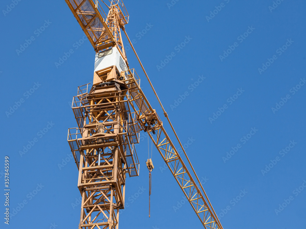 Yellow metal crane in front of a building being assembled in a construction site taken from below during a sunny afternoon, under a blue sky
