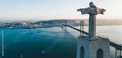 Aeria view monument Sanctuary of Christ the King. Drone flyby past near giant sculpture overlooking city of Lisbon Almada and famous 25th april bridge over river Tagus at sunset