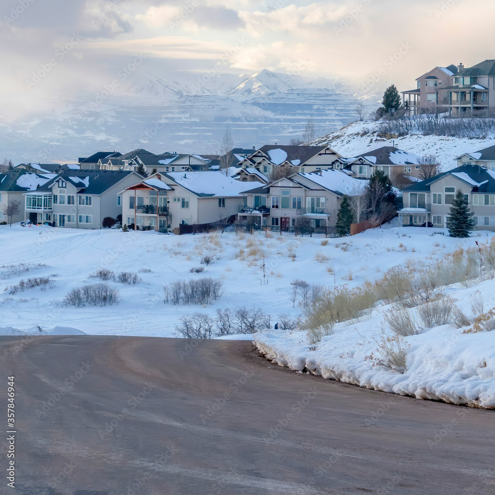 Square frame Curving road on snowy mountain setting with houses against cloudy blue sky
