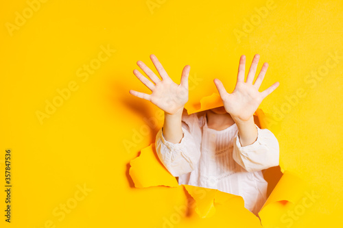 Child hands is showing ten fingers through a ripped hole in yellow paper, with copy space. photo