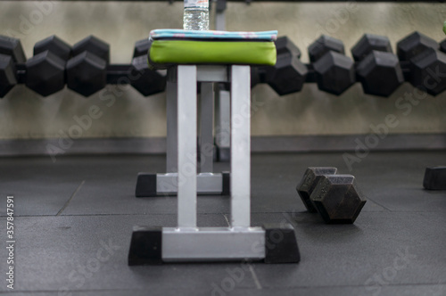 One black dumbbell near a training bench in the background on a specialized rack for dumbbells. Sport, fitness, weightlifting, healthy lifestyle. Exercise in the fitness room.