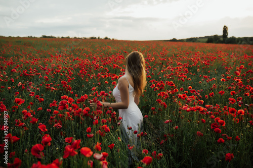 Tender woman in white dress standing in poppy field and enjoying beautiful landscape. Relaxing in nature during summer evening. Atmospheric authentic moment. Copy space.