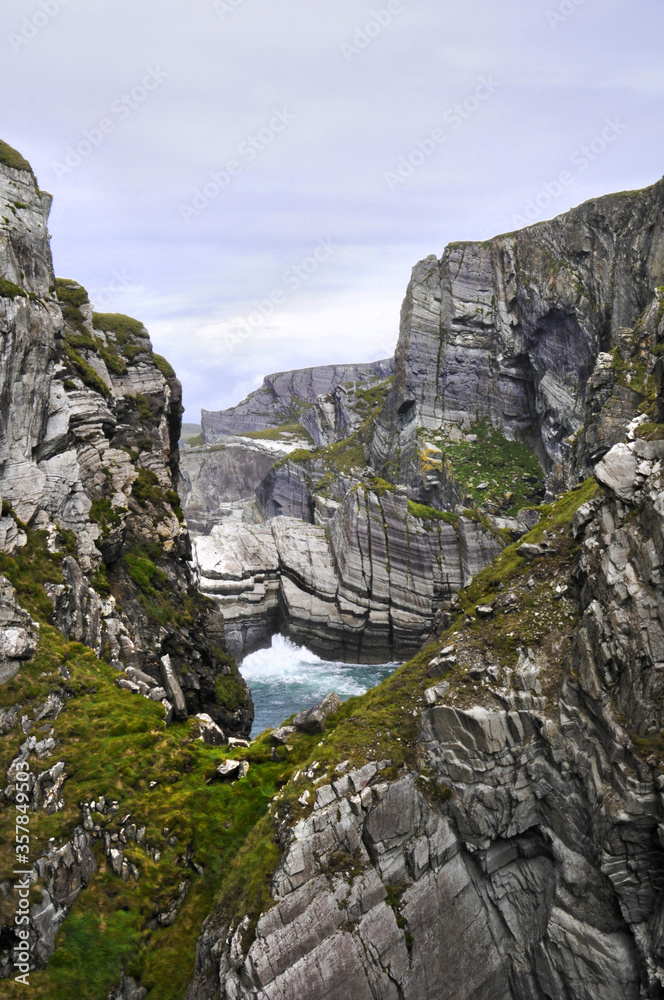 Vue panoramique sur les falaises de la pointe sud de l'Irlande. Mer, rochers, vagues et écume sur fond d'eau turquoise et phare à l'horizon.