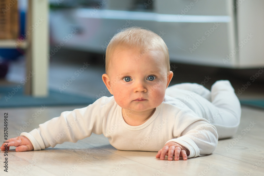 little baby crawling on floor at home, portrait of blond eight month baby lying on ground little baby crawling on floor at home, portrait of blond eight month baby lying on ground
