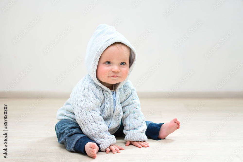 nine month baby sitting on floor and smiling, baby boy in hood at home sitting in front of white wall, banner copy space, mother's day concept nine month baby sitting on floor and smiling, baby boy in hood at home sitting in front of white wall, banner copy space, mother's day concept
