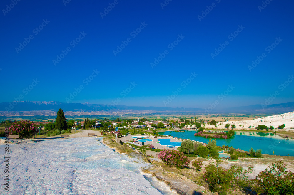view onto famous travertine terraces of Pamukkale, Turkey. Artificial lake with green and blue color at foot of structures. Town itself is on background. All natural objects included in UNESCO