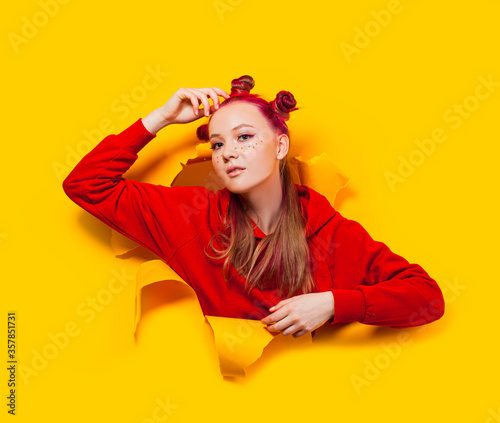 Teenage girl sticking out of torn hole in a yellow paper wall