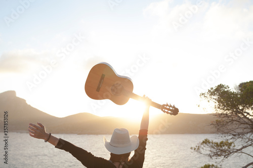 Arafed woman with guitar and hat standing on a cliff overlooking the ocean, by James Baynes, holding a guitar, women playing guitar, white straw flat brimmed hat, white cowboy hat, alan jackson photo