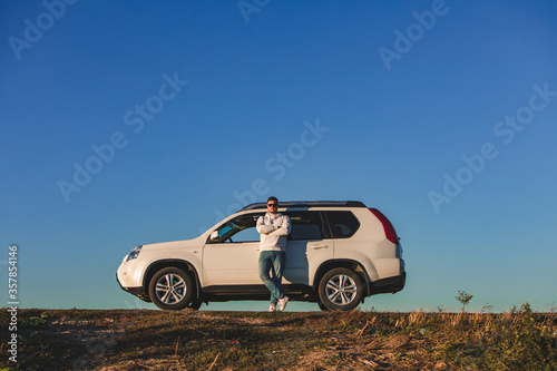 man standing in front of white suv on sunset. car travel concept © phpetrunina14