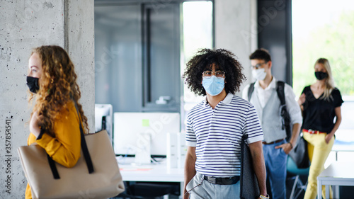 Young people with face masks back at work in office after lockdown, walking.