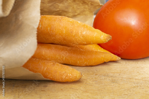 Fresh organic carrots in recyclable bag and red tomato on wooden background. Healthy food, vegetarian.  Vegetables  from super market.
