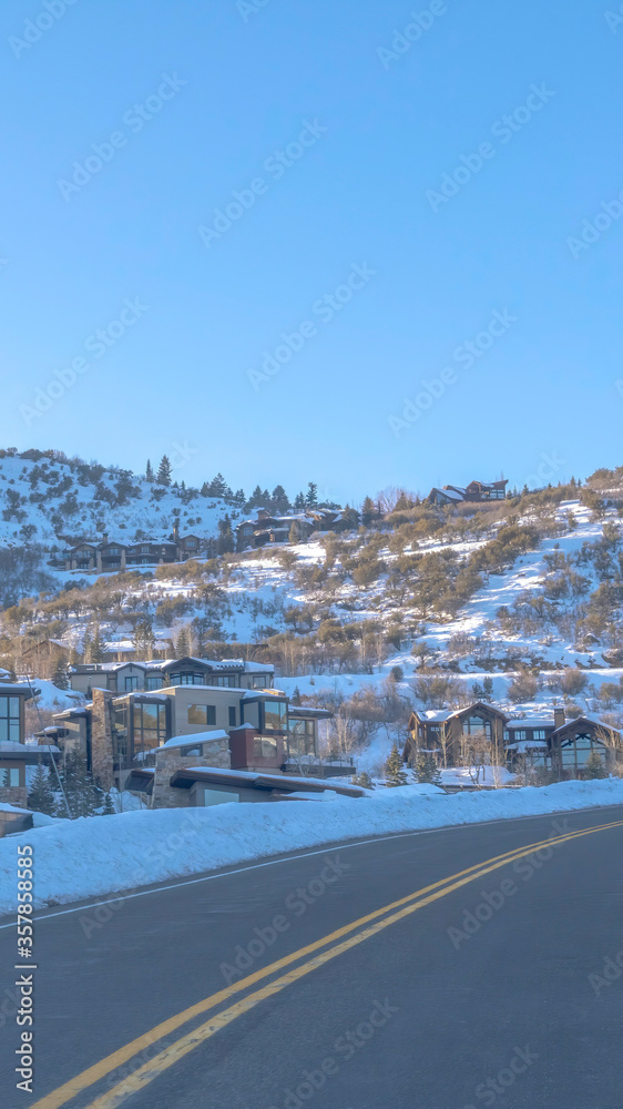 Vertical crop Road in Park City passing along snowed in mountain slopes with homes and trees